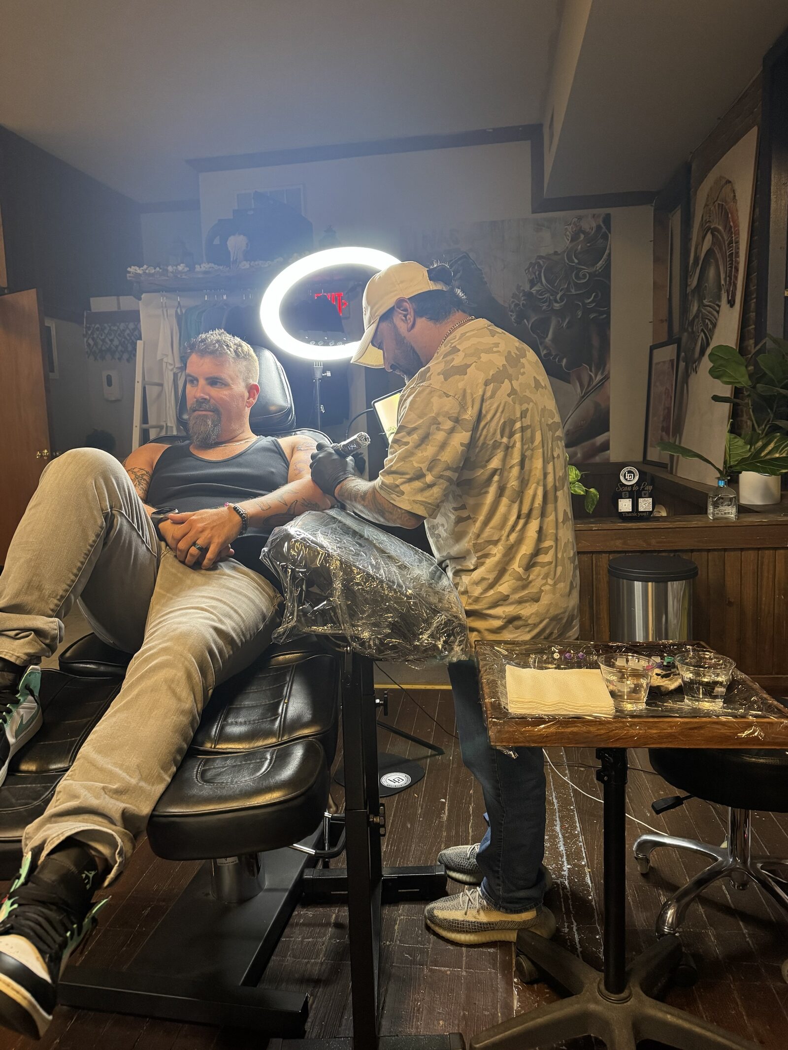Jeremiah tattooing a client’s arm under a ring light in the studio.