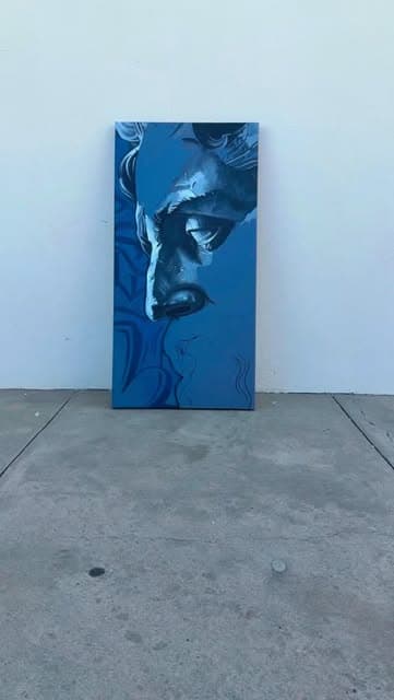 A tall blue portrait painting leaning against a white wall.